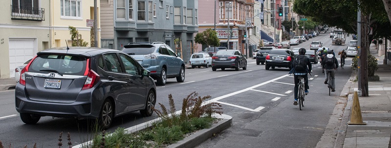 Bikes and cars traveling down the street.