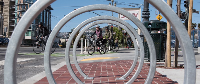 Bikers riding past a bike rack.