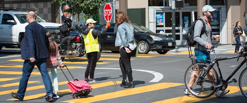 People crossing the street with the help of a crossing guard.