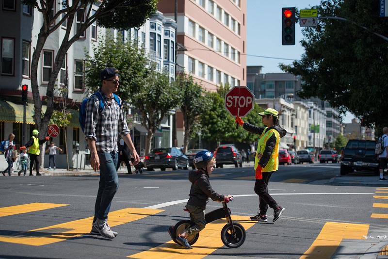 A crossing guard helping a father and son cross the street.