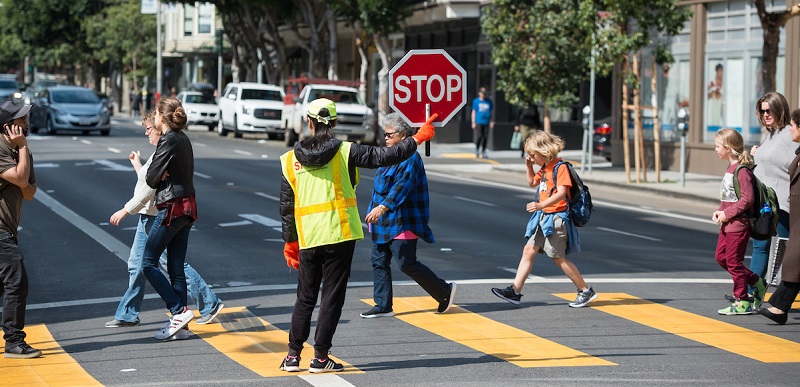 People crossing the street with the help of a crossing guard.