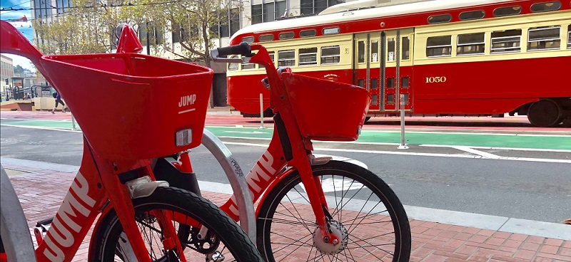 Two JUMP Bikes parked by a historic trolley. 