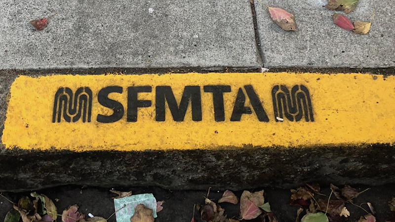 Painted yellow curb with stencil that says "SFMTA"