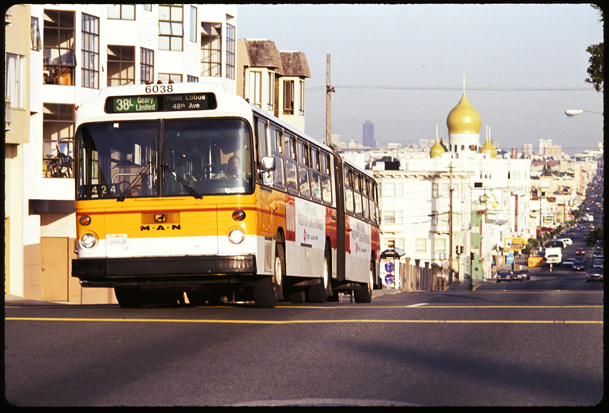 Articulated bus cresting hill on Geary Boulevard with city in background.