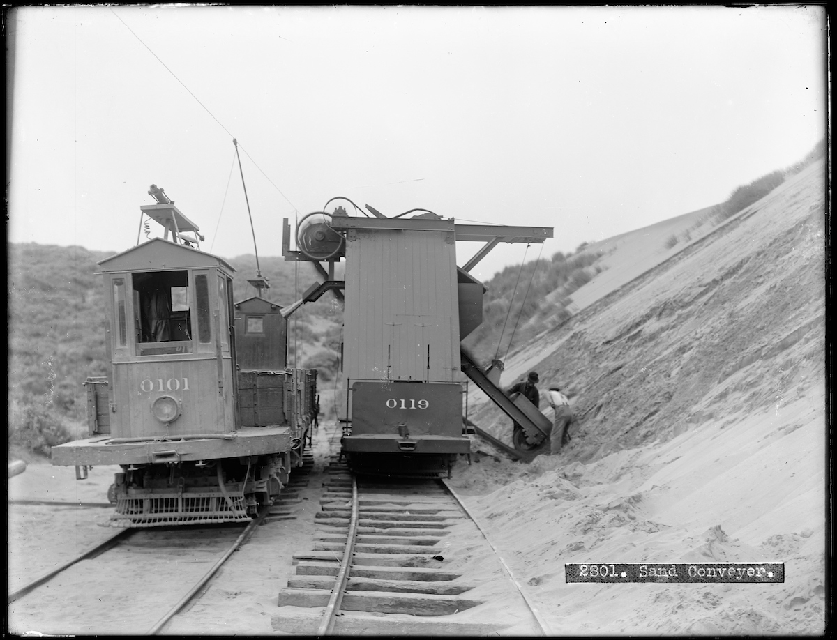work streetcars in between two sand dunes with men shoveling sand