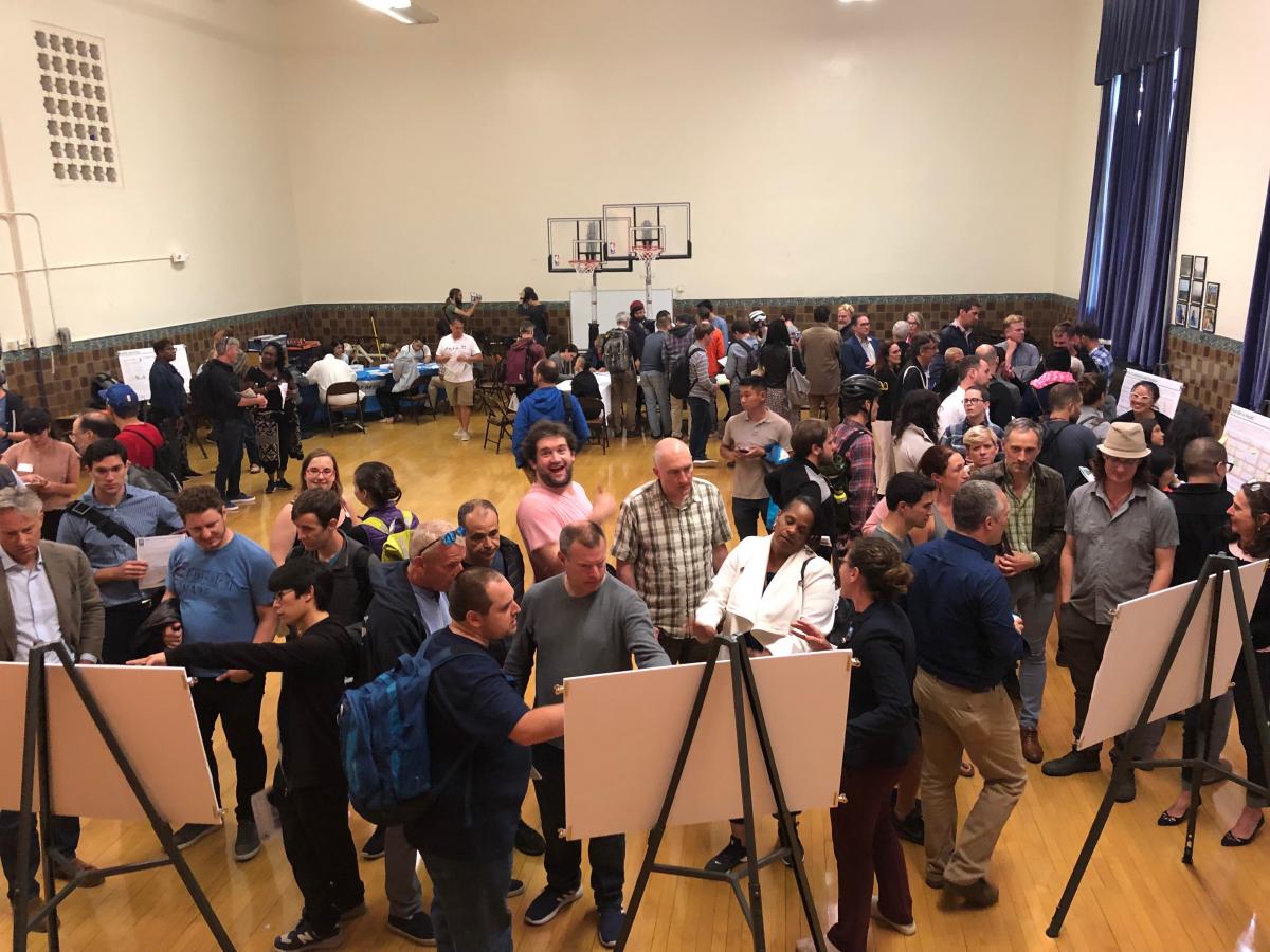 Photo of attendees reviewing and discussing project materials with staff in a school auditorium