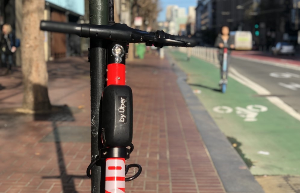 A scooter chained up and a scooter being ridden on the bike path.