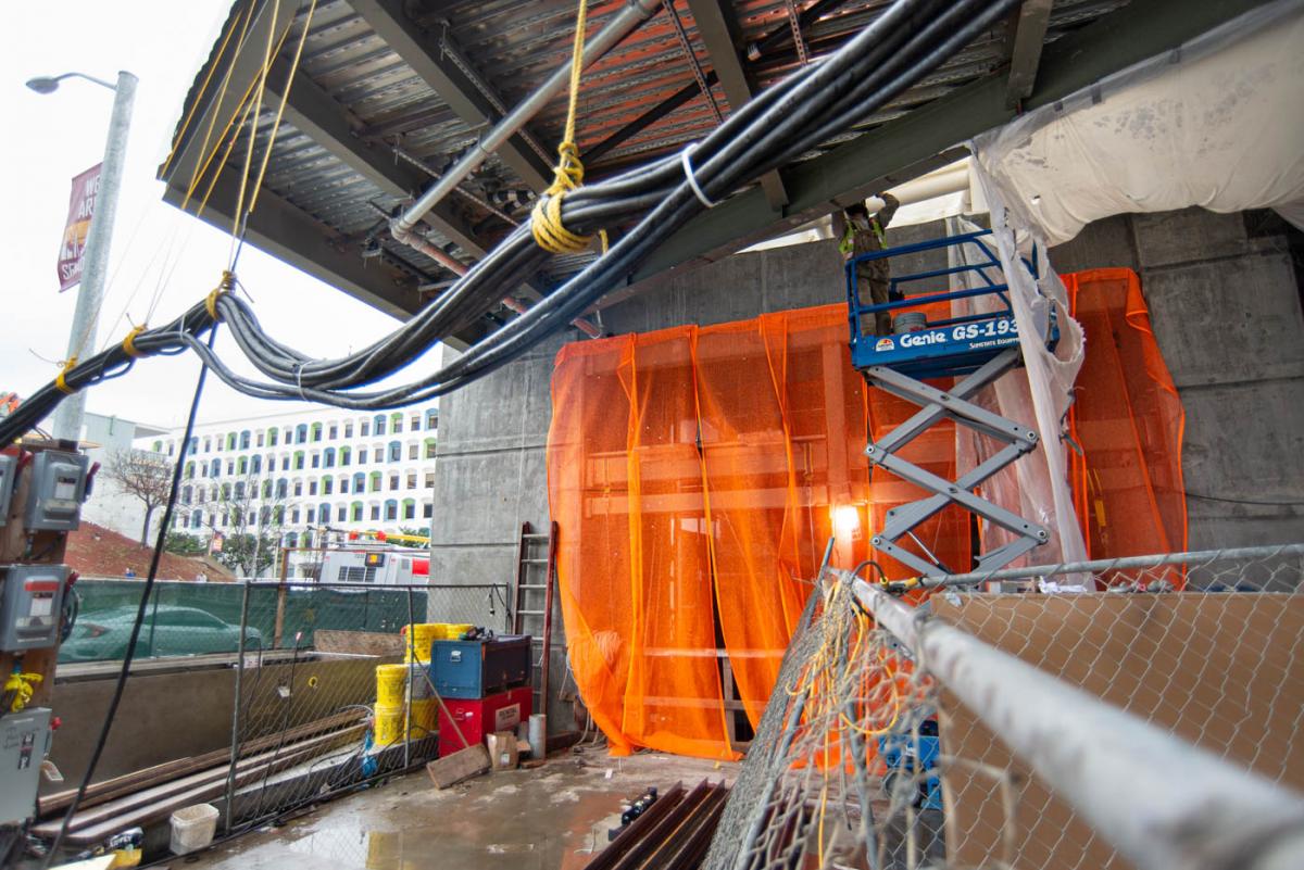Orange mesh covers future street-level elevator shafts near a worker installing pipes for the fire suppression system.