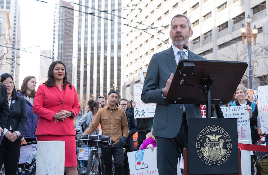 Better Market Street opening day speaking program with downtown buildings and Muni wires in the background