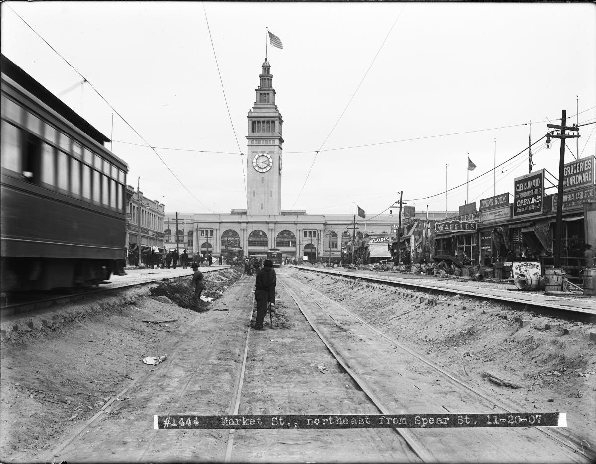 work men standing in sunken road with ferry building in background.