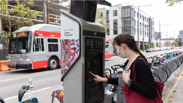 Woman uses bikeshare station while Muni 22 bus drives past