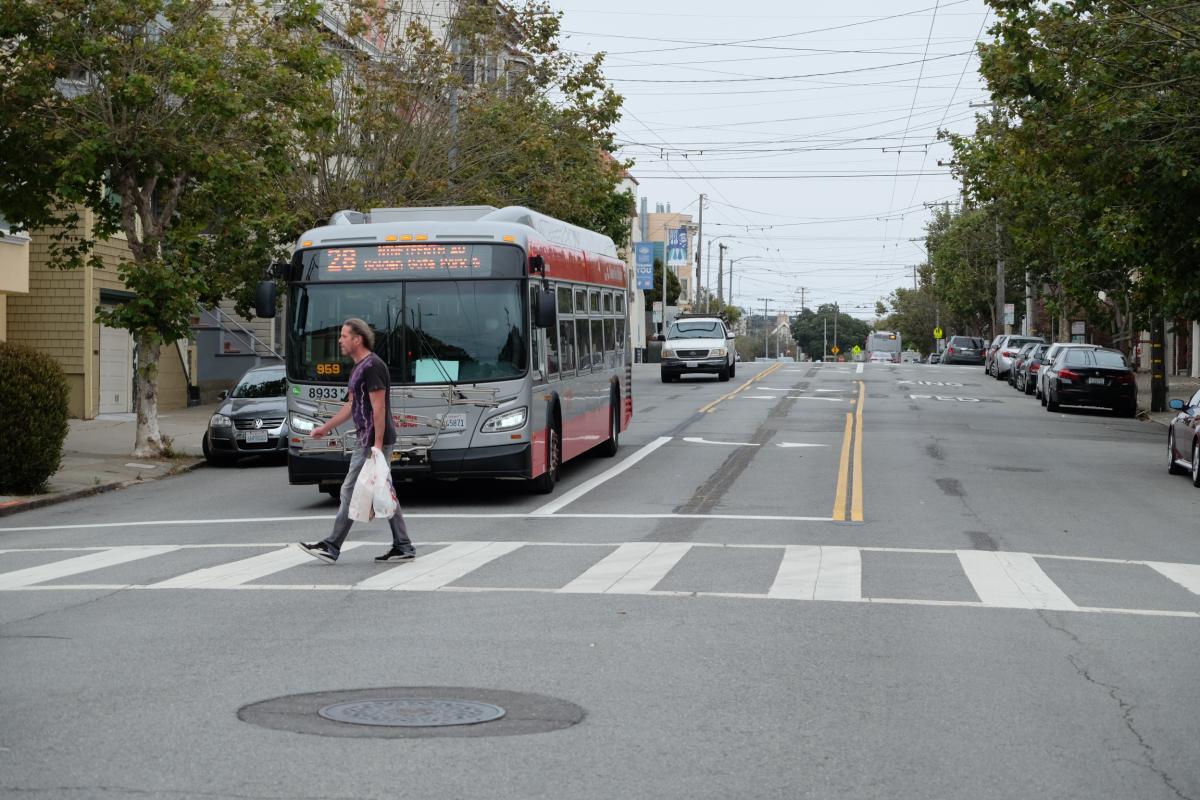 Man walking in crosswalk in front of a bus