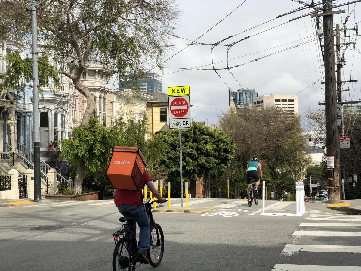 Image of one road cyclist and one food courier headed eastbound on Page Street through the new diverter at Laguna Street