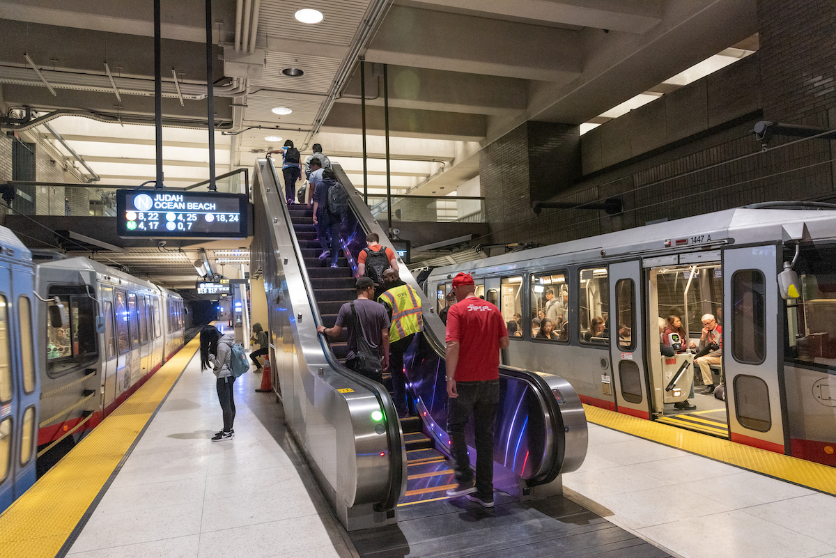 view of Van Ness Station escalator and platform with people and train