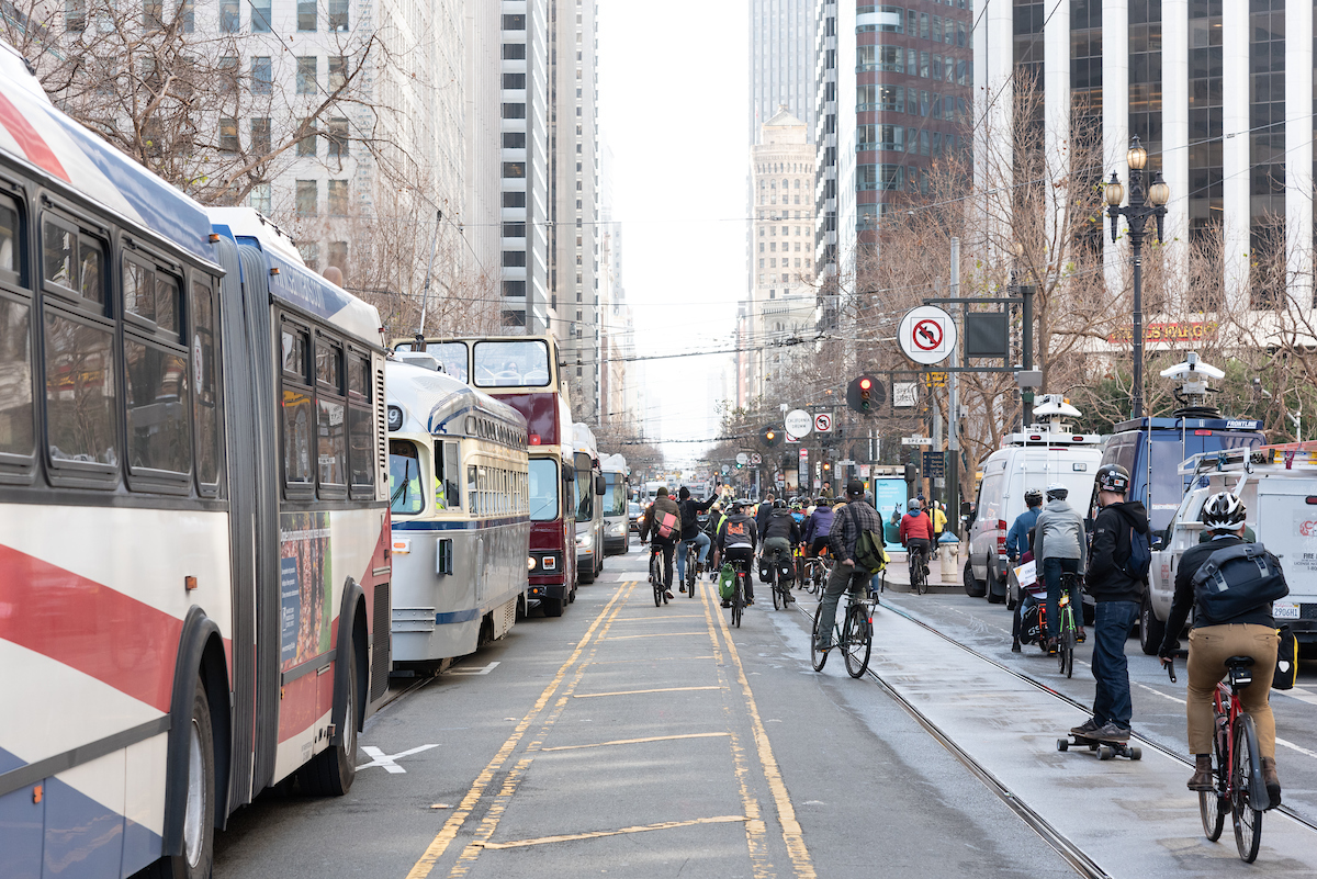 Buses and trams line Market Street near Embarcadero as many people bike and skateboard on the newly car-free stretch of road.