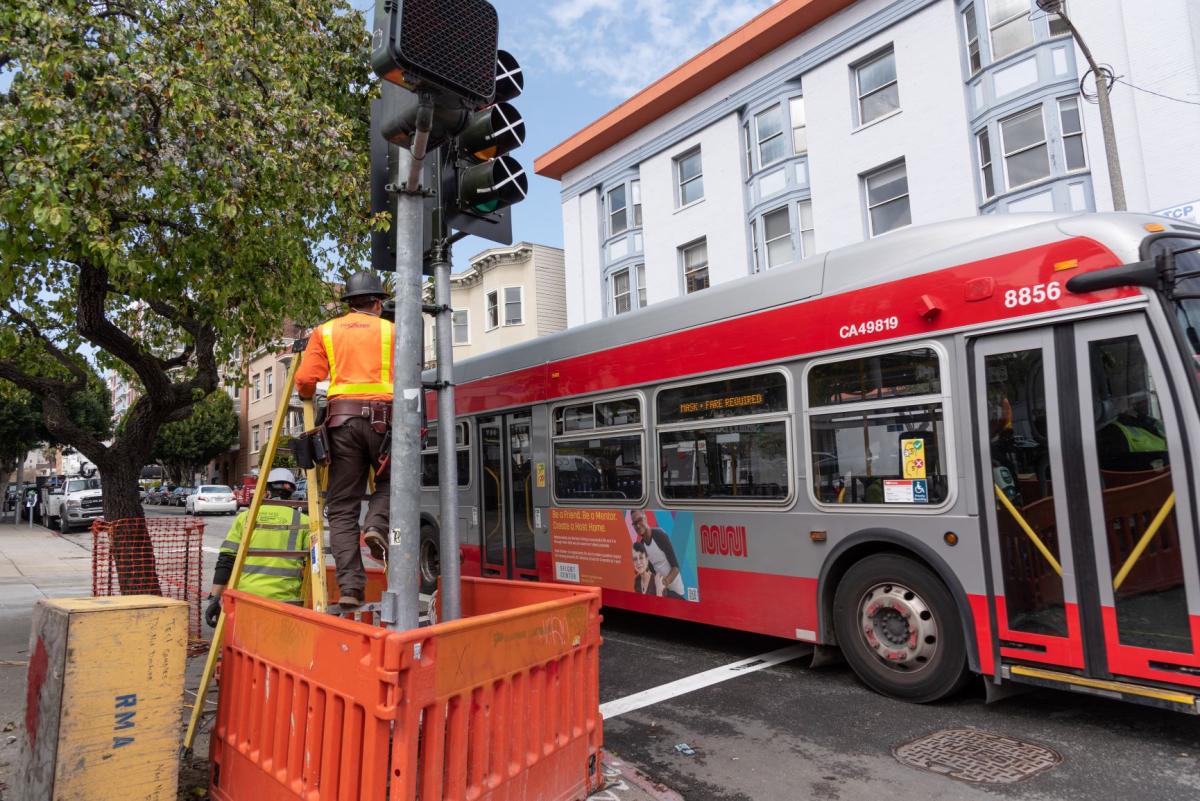 Workers installing pedestrian count-down timers at northeast corner of Pacific and Van Ness.