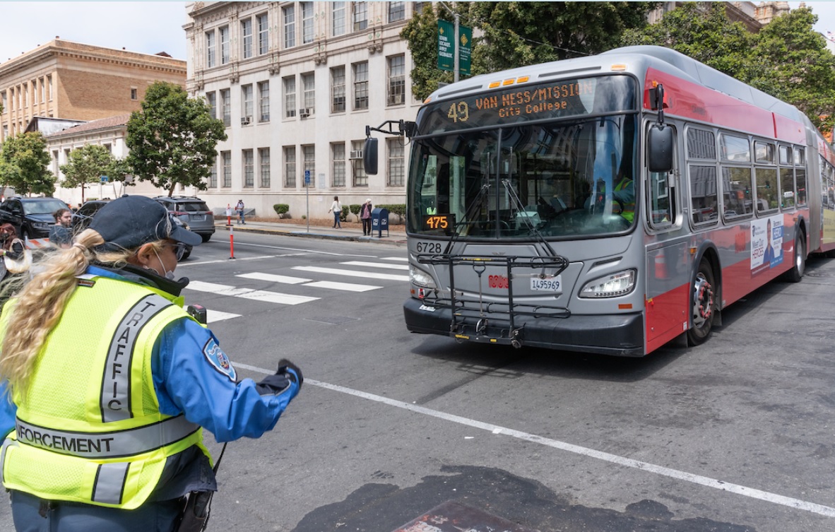 Photo of a traffic control officer guiding a 49 Van Ness bus through an intersection