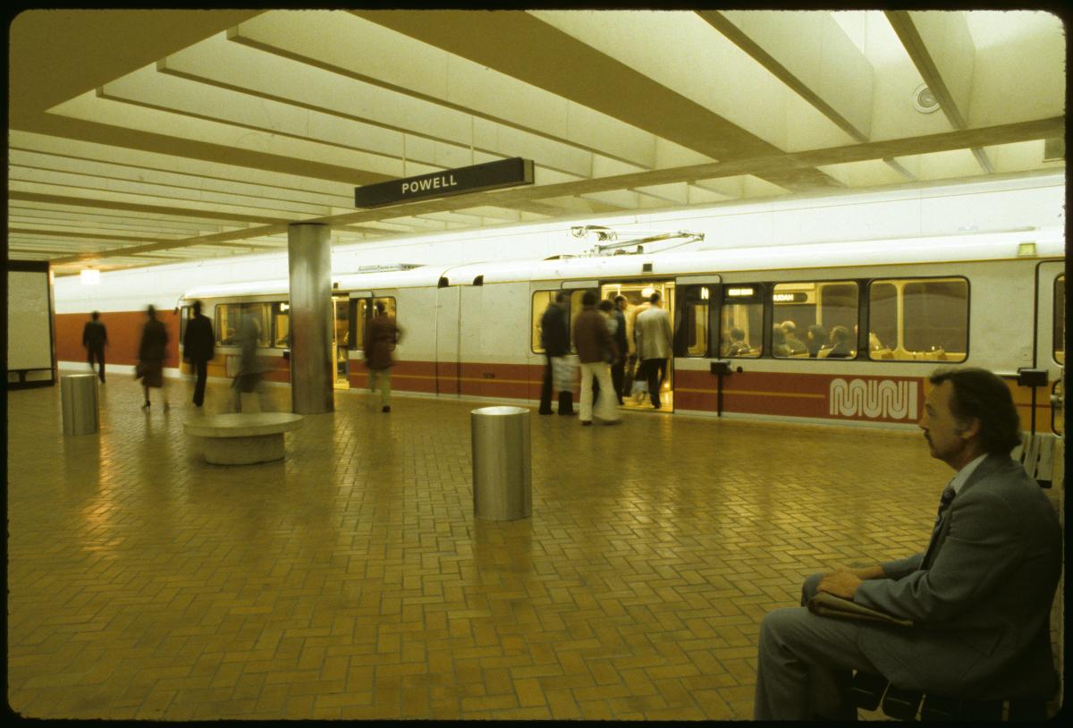 Man sitting in Powell Station as people board a Muni Metro