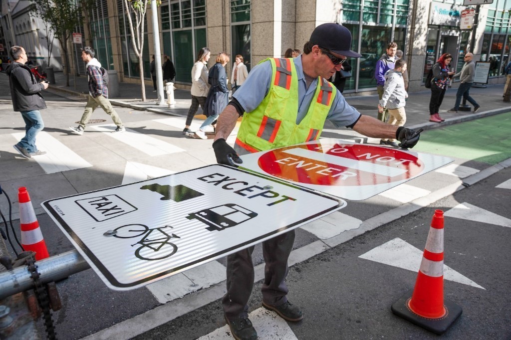 Photo of worker getting ready to put up a pole with new signs indicating that Market Street is restricted to non-private vehicles only.