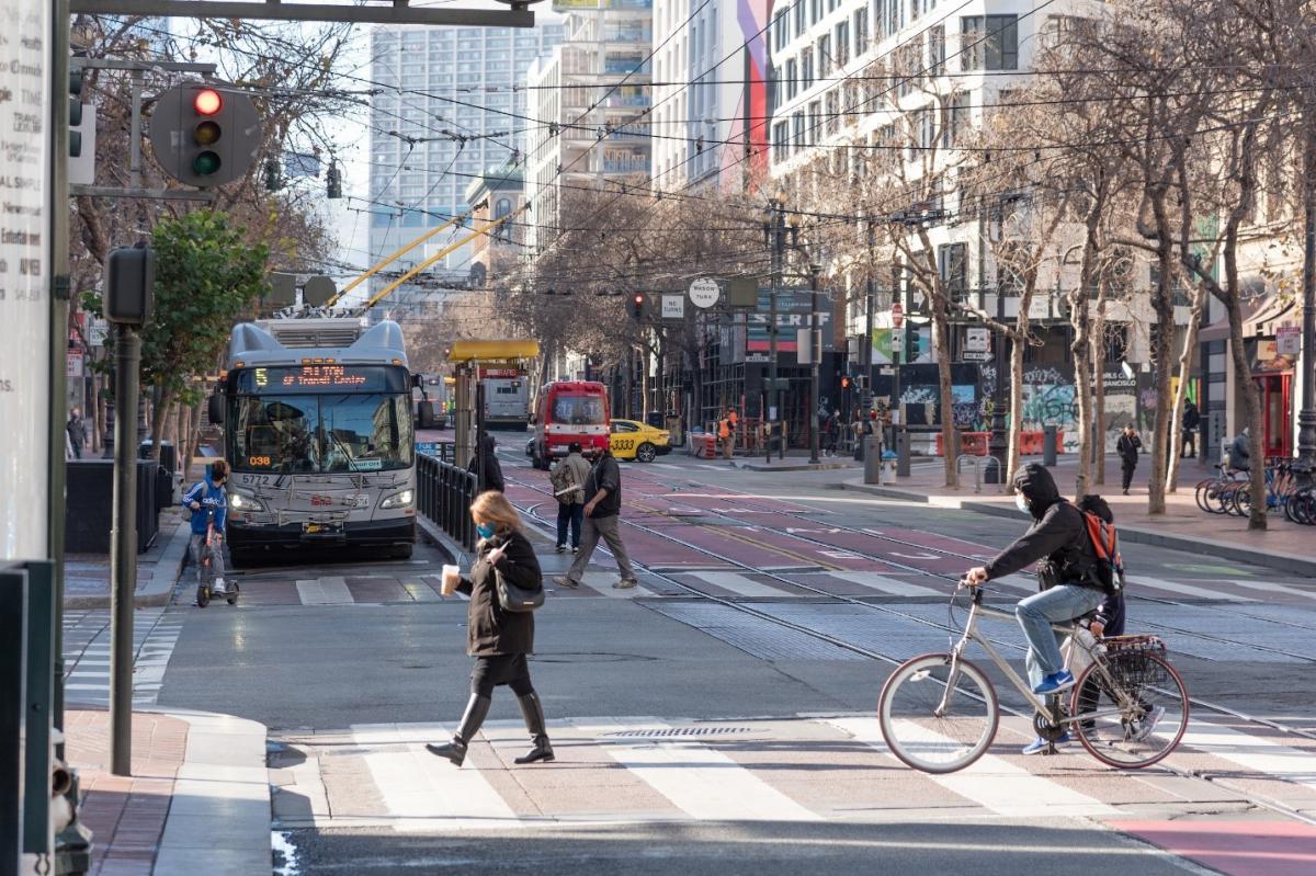 Photo of Market Street intersection with 5 Fulton bus, pedestrians, people on bicycles, a taxi, an ambulance, bikshare station, and powered scooter