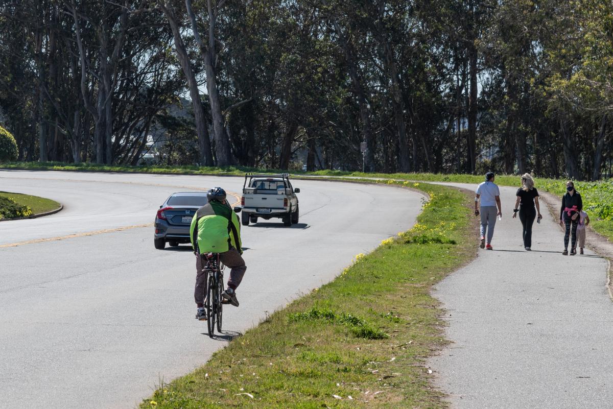Photo of people walking and biking, with cars passing by on Lake Merced Boulevard