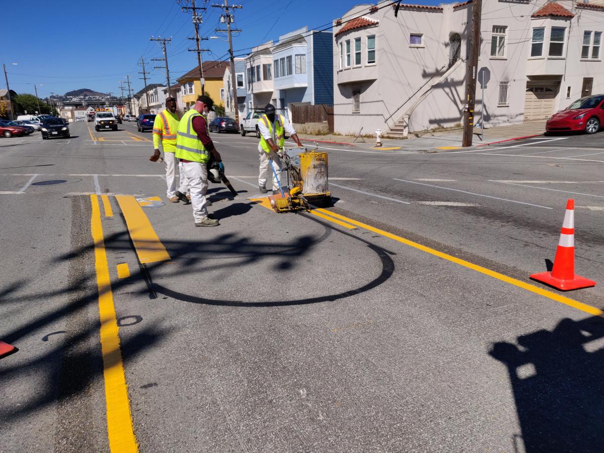Photo of three SFMTA Paint Shop workers restriping a roadway with new paint.