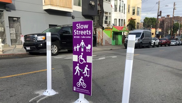 Image of three posts place in the travel lane with a sign indicating "Slow Street" in English, Chinese and Spanish