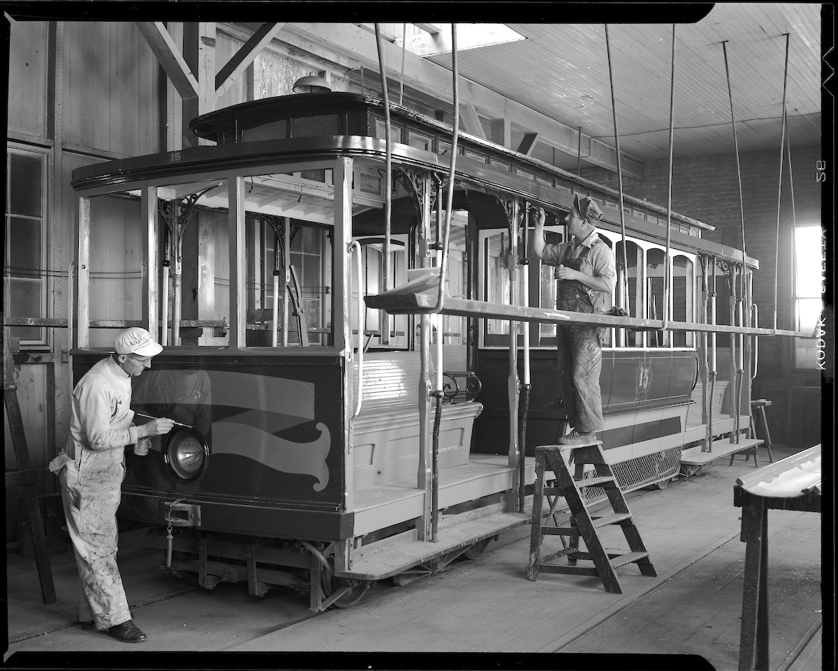Two painters work on California Street Cable Car 15 in the paint shop 
