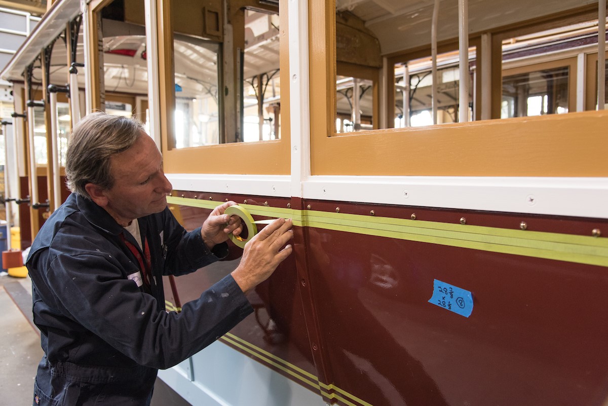  A painter lays down masking tape to paint striping on the side of Powell St. Cable Car 22,