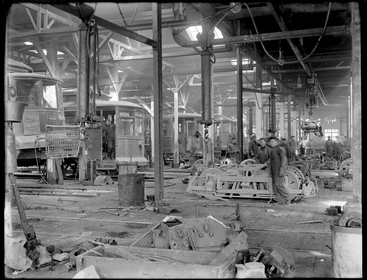 A view inside the overhaul shop in 1912 showing a row of streetcars at left and staff tearing down trucks and motors at right.