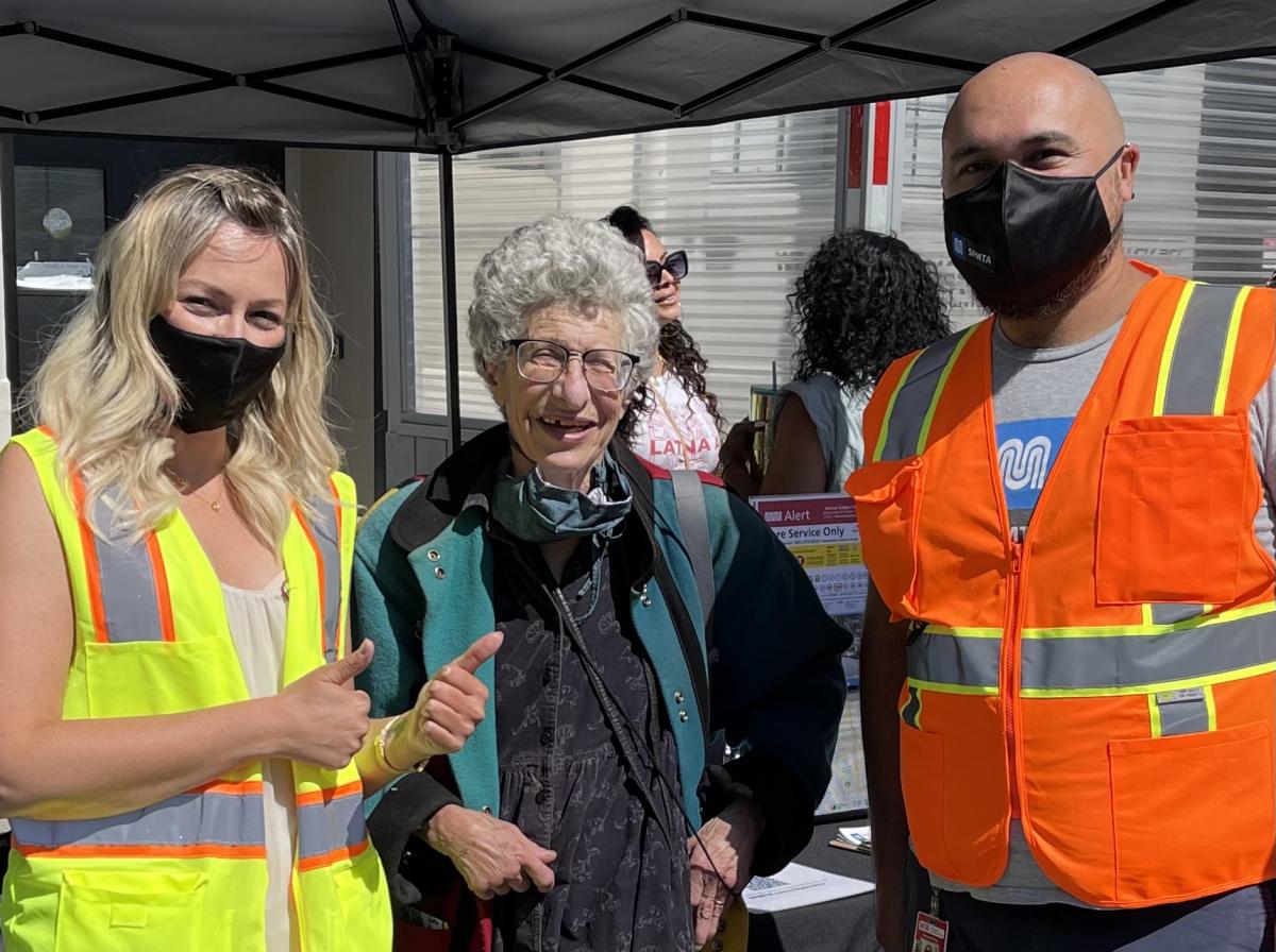 Two SFMTA staff pose for a photo with a long-time Muni customer at Carnaval SF 2021.