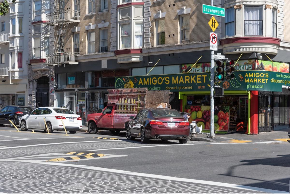 On Leavenworth Street, a car navigates a left turn through the intersection; there are small rubber speed bumps in the road directing the turn, as well as plastic delineator posts down the median at the intersection