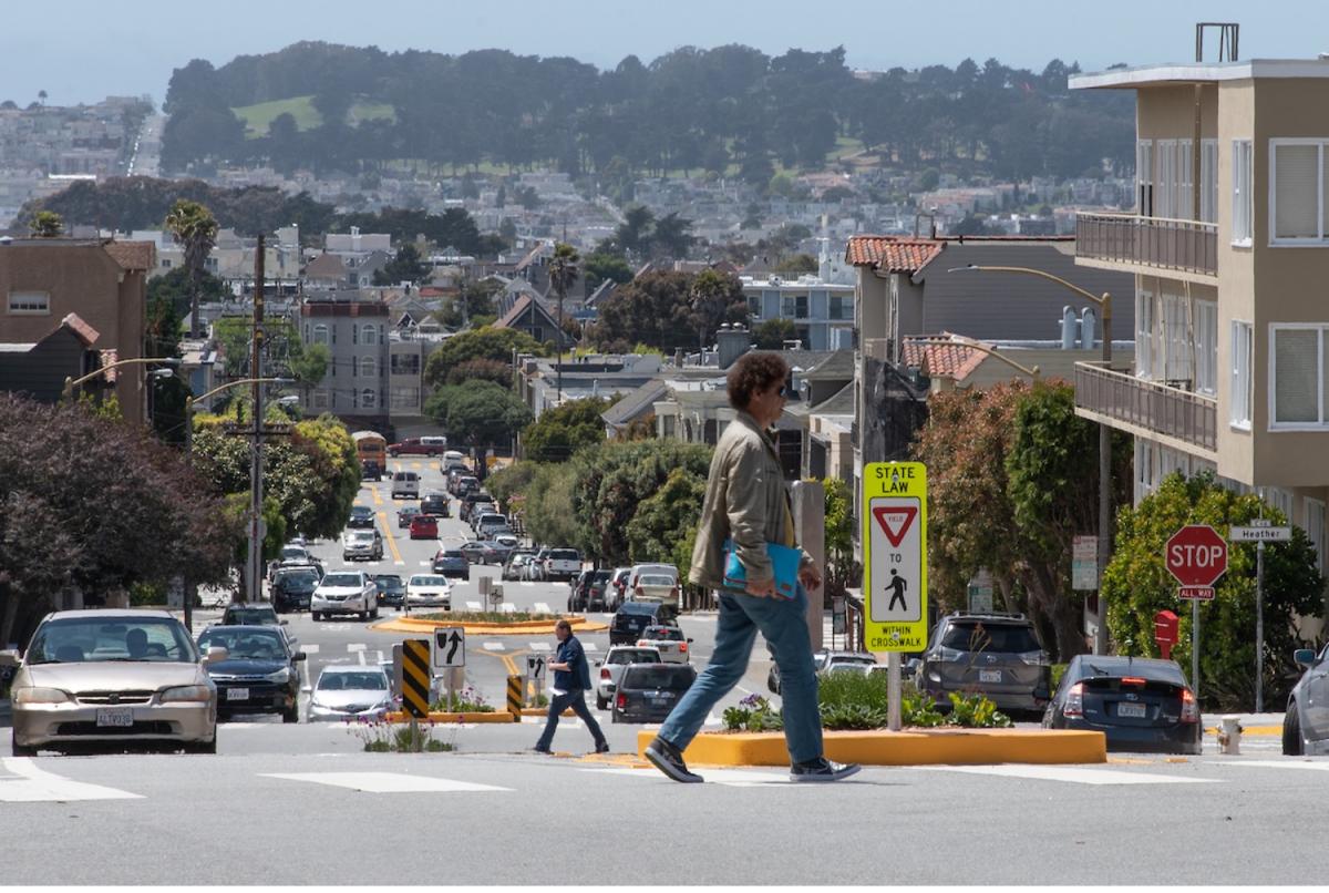 People cross Heather Street, where there's a pedestrian refuge island in the middle of the street