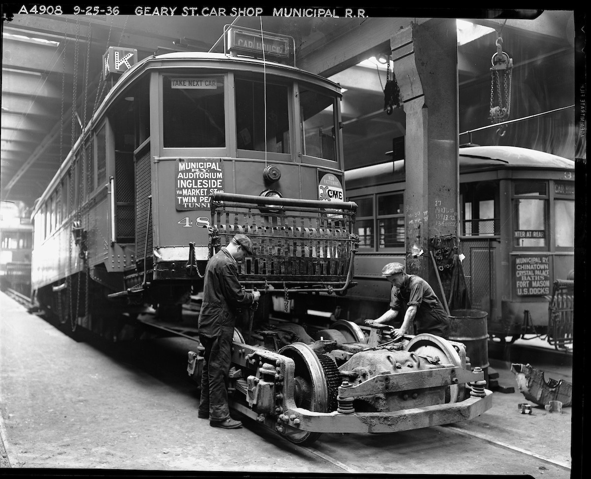 Inside the shops at Geary Car House, two mechanics work on a truck (the combined wheels, suspension, and motor of the streetcar) pulled from a K Line streetcar in this 1936 photo.