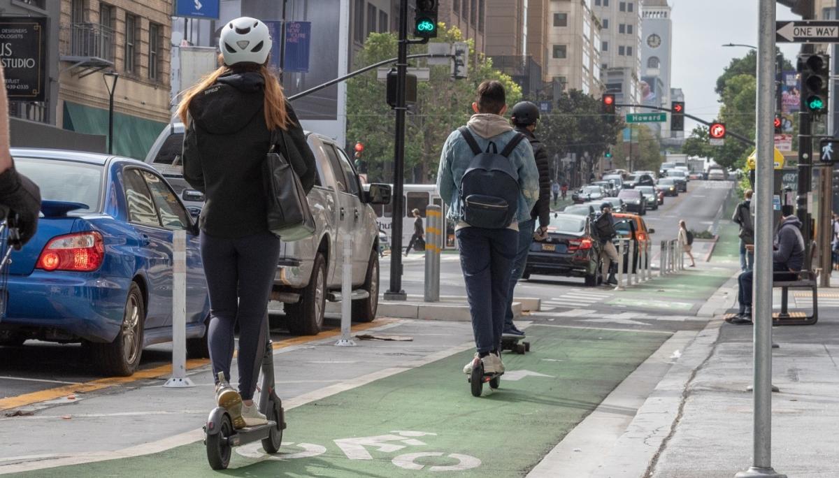 Photo of two powered scooter riders, a skateboard user, and pedestrians