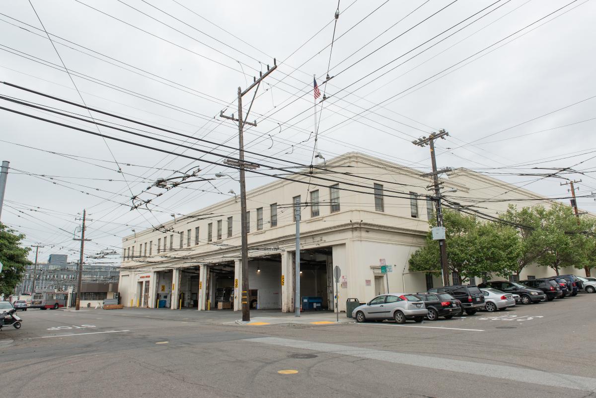 Bus yard entrance shown with parked cars along the building side up the hill