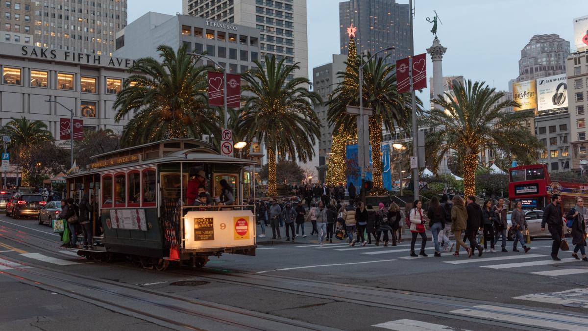 A filled Cable Car at a busy intersection in Downtown San Francisco decorated in holiday festivities with dozens of shoppers and vehicles 