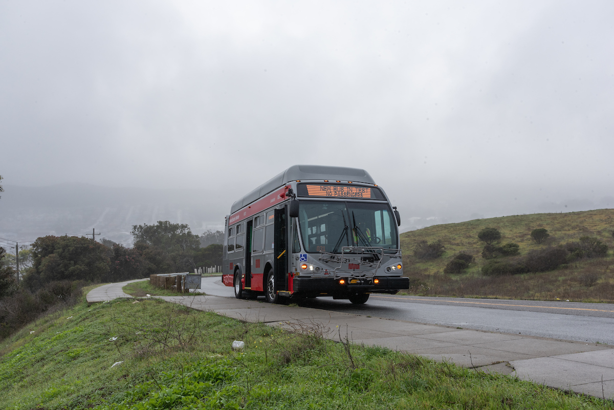 Muni bus parked on street with fog and hills behind.