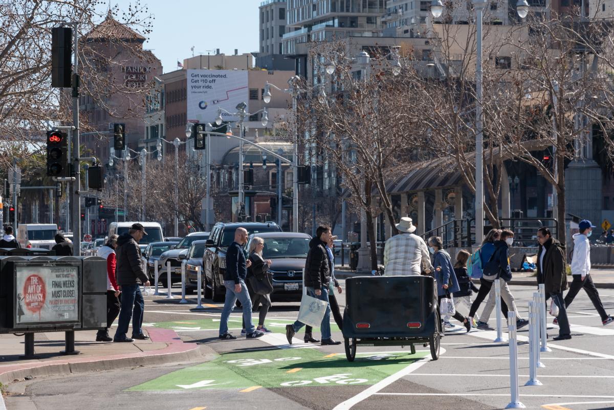 Image of people crossing in a newly-striped crosswalk on The Embarcadero near the Ferry Building with a pedicab waiting at a bicycle traffic signal