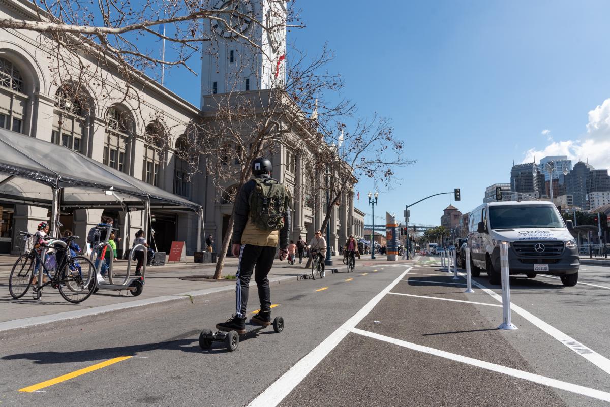 Image of people bicycling and riding an electric skateboard in the new two-way bikeway on The Embarcadero in front of the Ferry Building