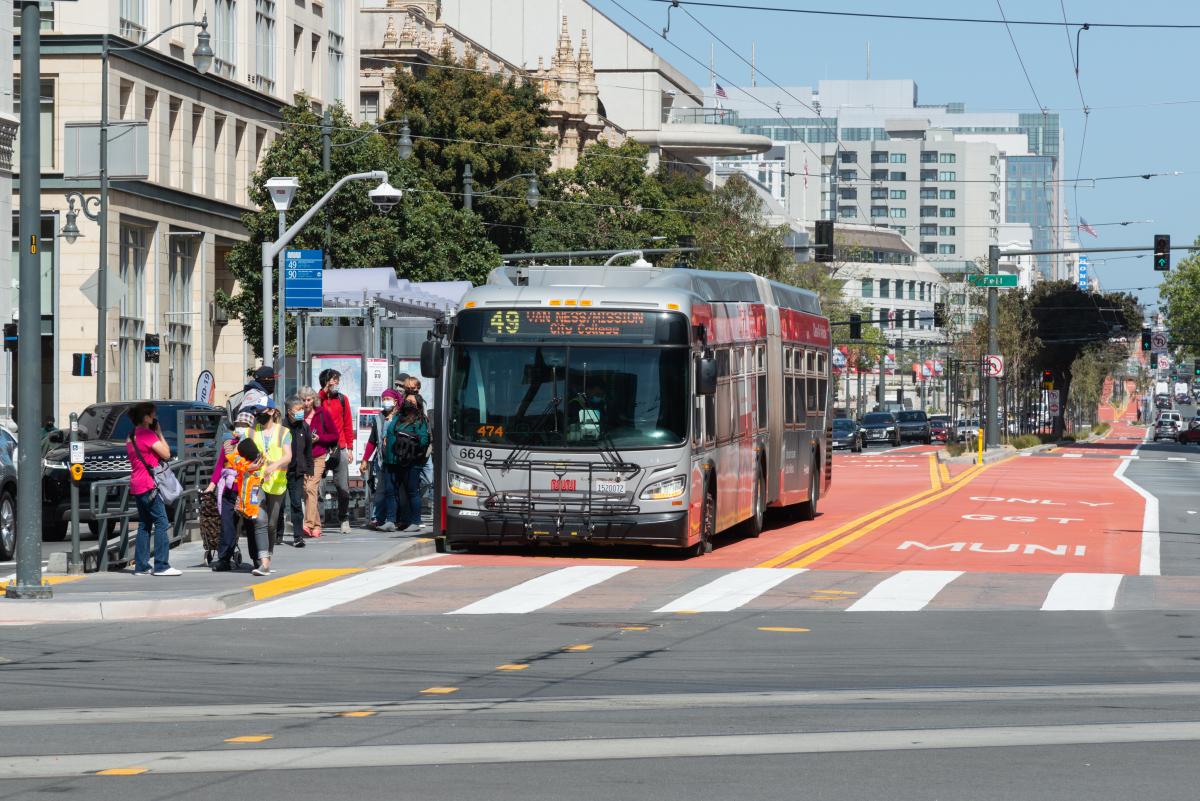 Muni bus stopped at intersection and unloading passengers at bus stop. 