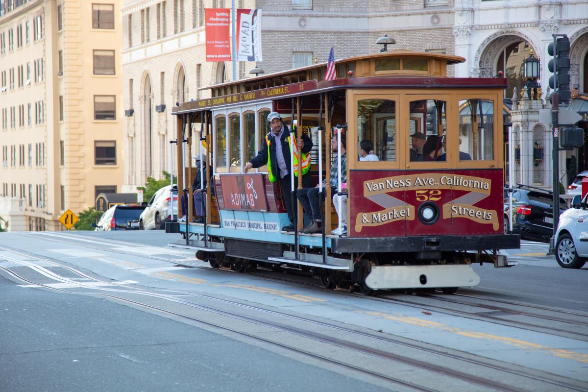 Cable car on a downtown street with a crew member hanging alongside 