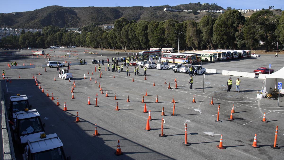 Cones in pattern formation on a parking lot with parked buses, parking enforcement vehicles and people 