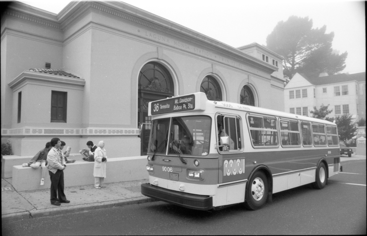 bus with people standing on sidewalk, forest hill station, and fog-covered trees in background.
