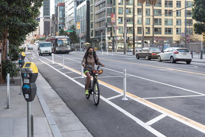Woman riding in a protected bicycle lane with Muni buses and other vehicles in adjacent lanes