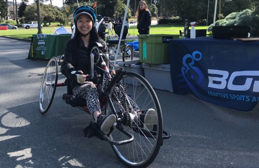 A woman sits on an adaptive recumbent bike in Golden Gate Park; a sign for BORP is in the background.