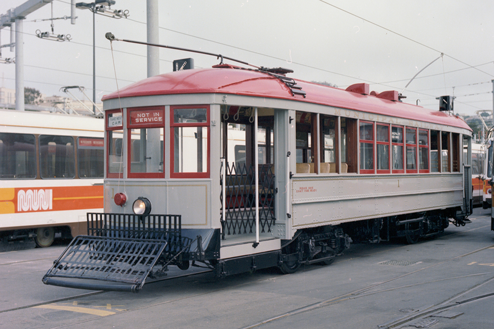 Color photo from 1980 of Muni streetcar 1 painted grey with a red roof and windows.