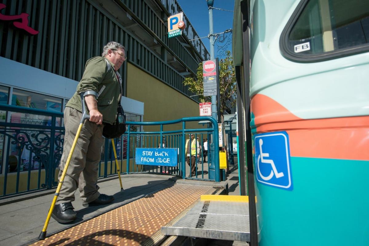 Bob Planthold boarding the F train via an accessibility ramp in his signature bright yellow crutches 