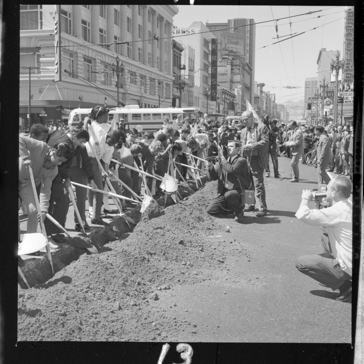 Black and white photo of a line of people digging with shovels in shallow ditch on Market Street