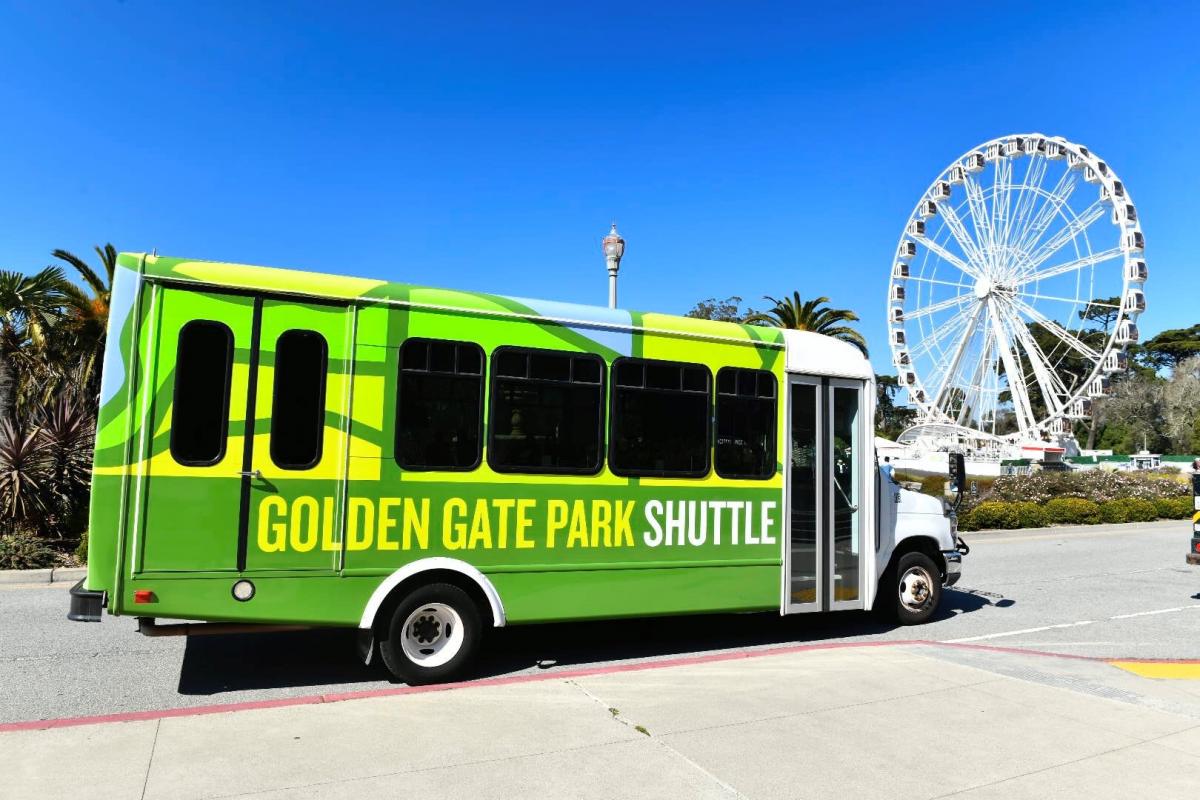 The Golden Gate Park shuttle is shown with the ferris wheel in the background. The sky is bright blue and cloudless.